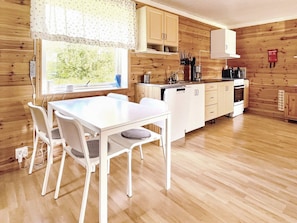 Cocina compacta con armarios de madera, encimera blanca y comedor con mesa y sillas.