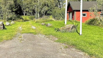 A red building with a gravel path leading to it, surrounded by greenery and rocks.