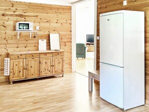 Una habitación con paredes de madera, un refrigerador blanco, un microondas y un mueble de madera con cajones.