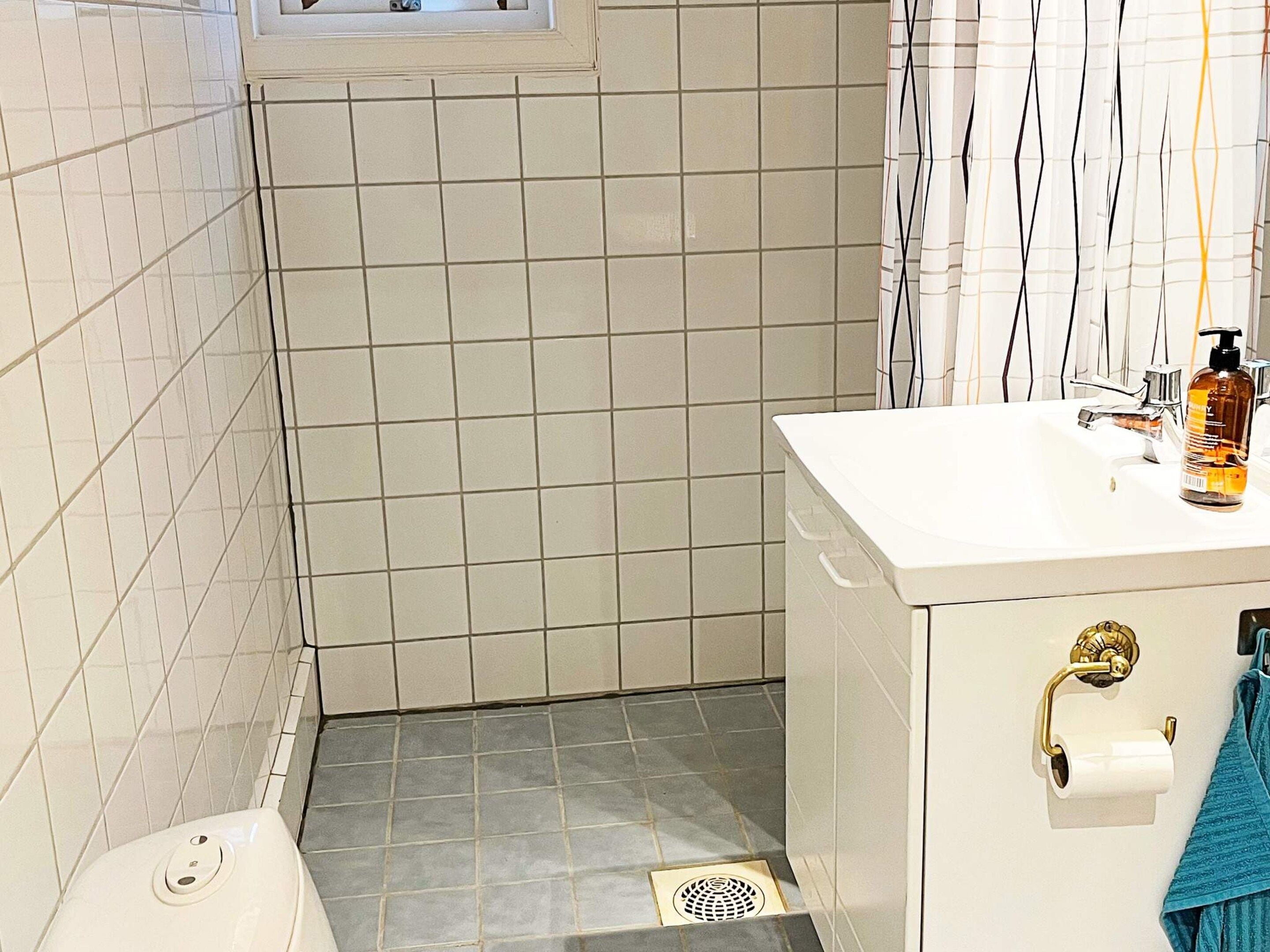 A bathroom with white tiled walls, a white sink with a gold faucet, a blue towel, and a bottle of soap.