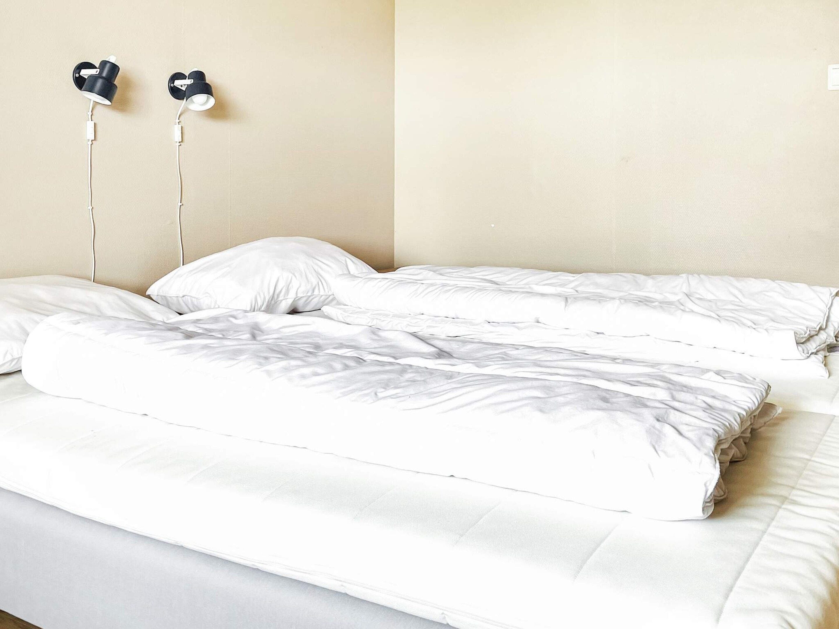 A bed with white bedding and two wall-mounted earphones.