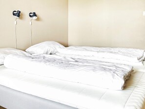 A bed with white bedding and two wall-mounted earphones.