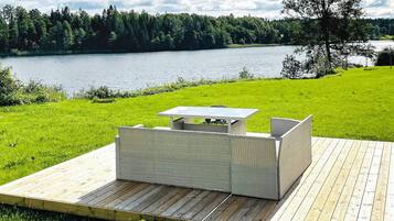 An outdoor deck with a table and chairs, overlooking a lake with a forested shoreline.