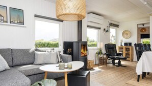 Ett mysigt vardagsrum med en grå soffa, ett runt bord, en svart öppen spis och en matplats med stolar och ett bord.