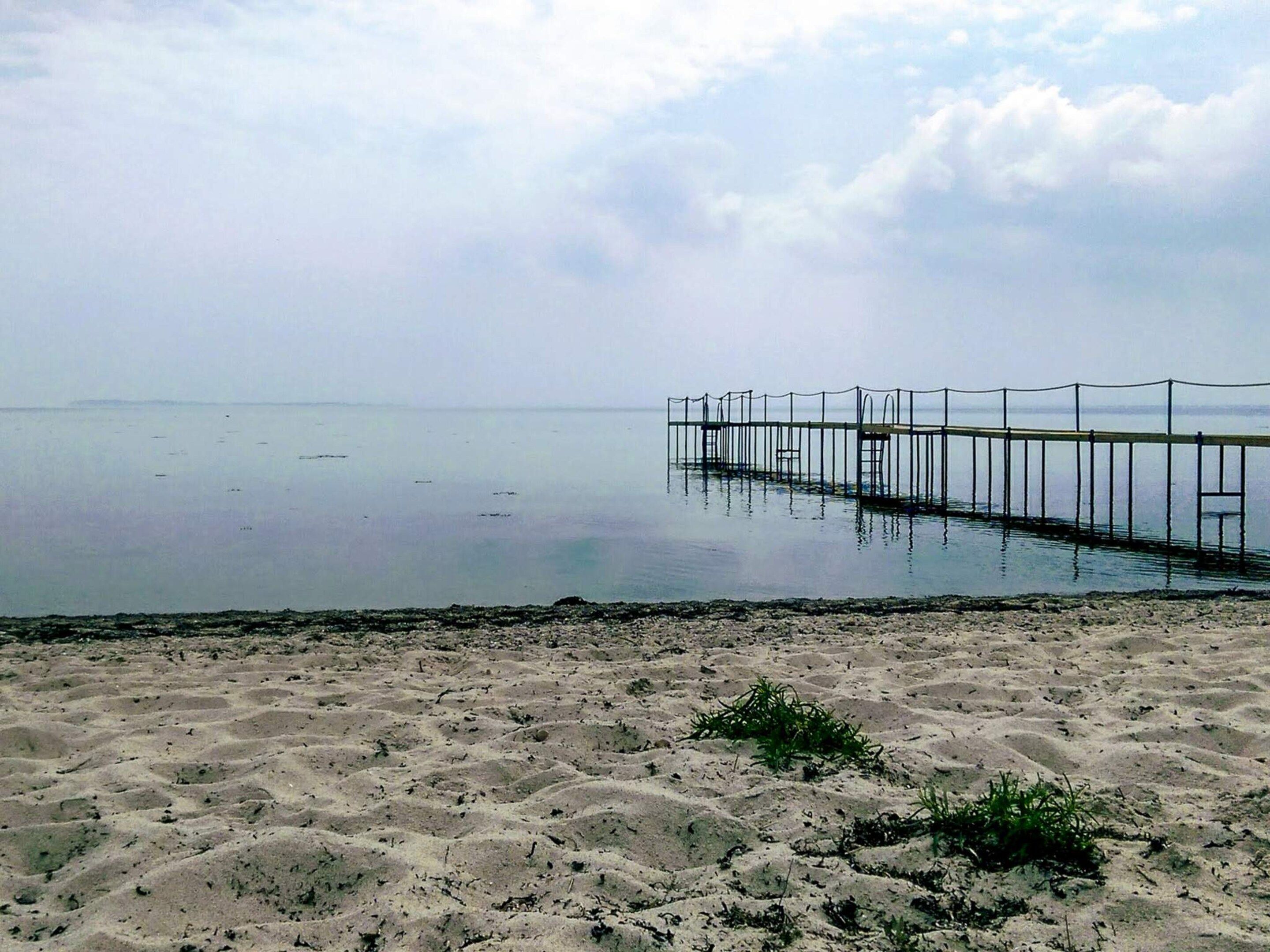 A beach with a wooden pier extending into calm waters.