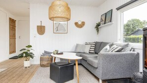 Ett mysigt vardagsrum med en grå soffa, ett runt soffbord, en svart pall och en flätad hänglampa.