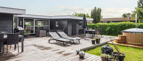 A modern outdoor deck with lounge chairs, a table, and a hot tub.