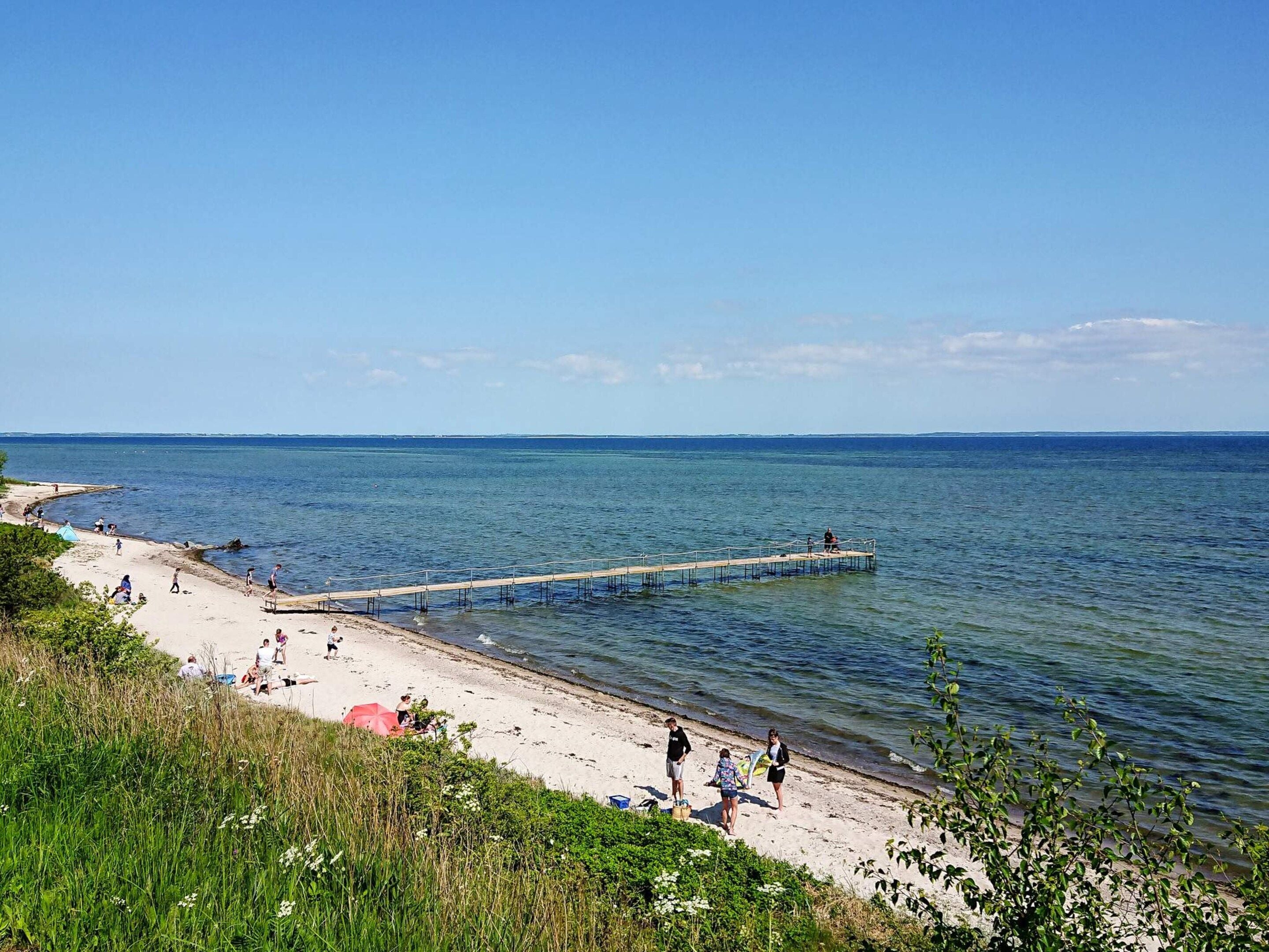 A beach with a pier extending into the water, people walking along the shore, and a clear sky.