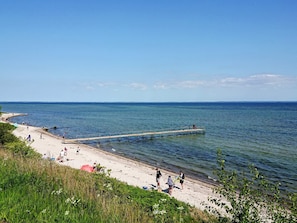 A beach with a pier extending into the water, people walking along the shore, and a clear sky.