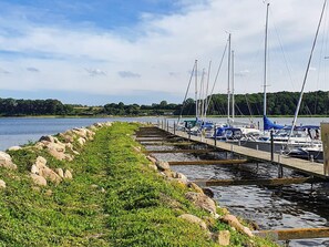 A marina with boats docked, a wooden pier, and a grassy area with rocks.