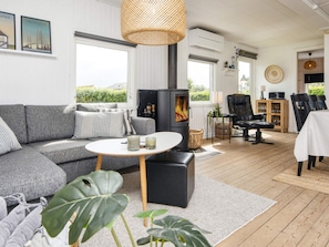 A cozy living room with a grey sofa, a round table, a black leather chair, and a wood-burning stove.