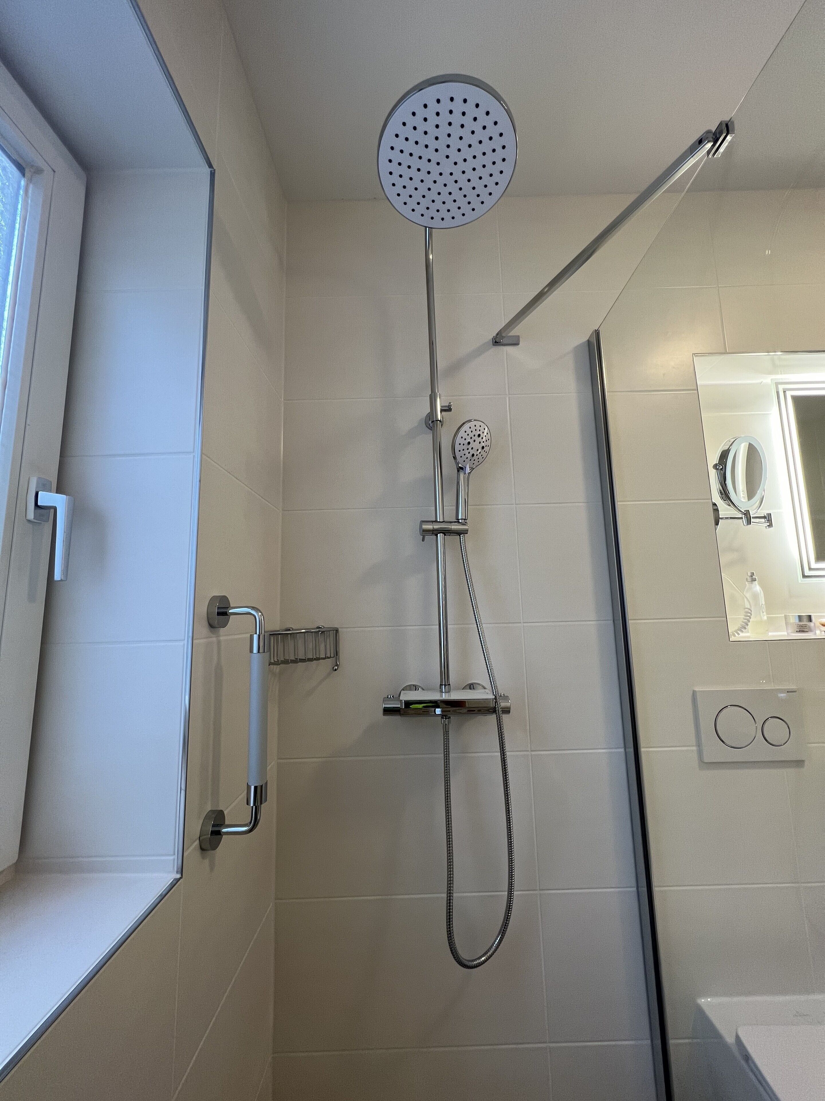 A modern bathroom with a shower, a handheld showerhead, a handheld shower nozzle, and a wall-mounted control panel.