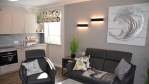 Una sala de estar moderna con un sofá y sillones, una mesa de centro y una cocina al fondo.