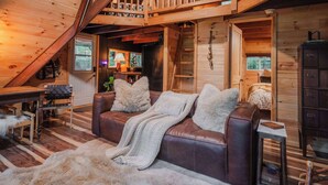 Un intérieur de chalet chaleureux avec une chambre à coucher en mezzanine, des poutres en bois, un canapé en cuir et un tapis en fourrure.