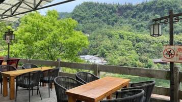 An outdoor seating area with tables and chairs, overlooking a forested valley.