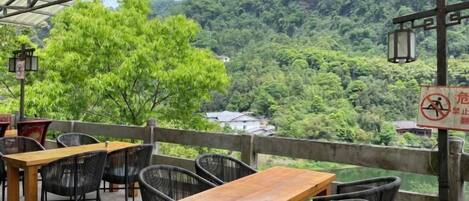 Un espacio al aire libre con mesas y sillas, con vistas a un valle boscoso.