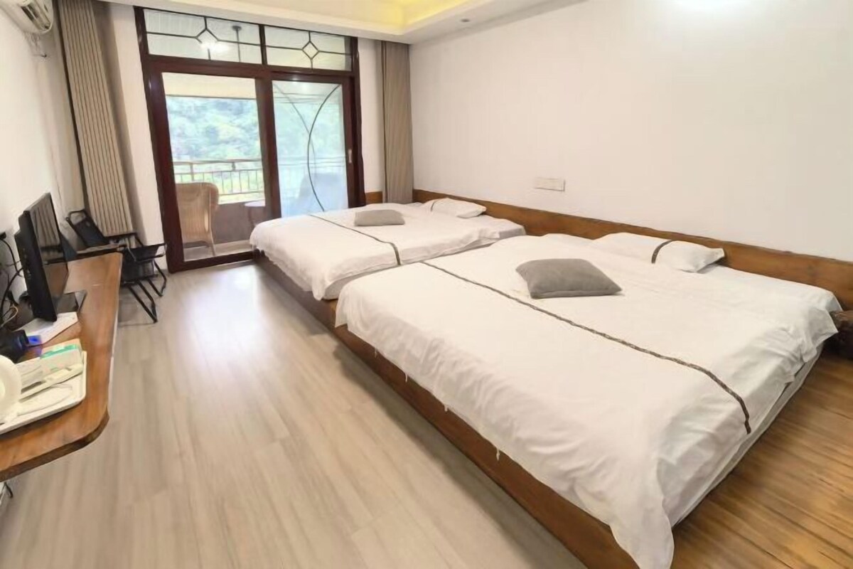 Een hotelkamer met twee bedden, een bureau met stoel, en een groot raam met uitzicht op groen.