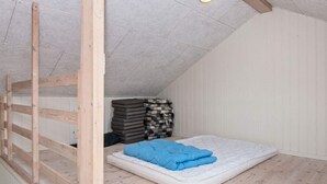 A loft bedroom with a sloped ceiling, a wooden ladder, a mattress with a blue blanket, and a stack of pillows. - 10 Person Holiday Home in Ronde (Ronde)