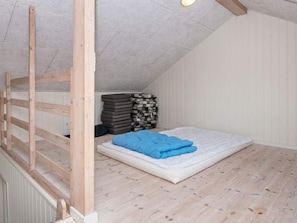 A loft bedroom with a sloped ceiling, a wooden ladder, a mattress with a blue blanket, and a stack of pillows.