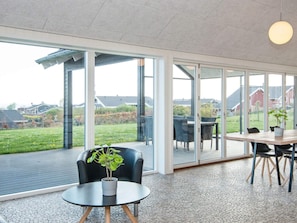 Interior moderno com grandes portas de vidro que dão para um jardim, uma mesa redonda com cadeiras e um vaso de planta.