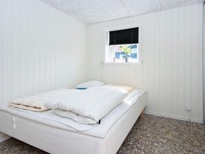 Quarto individual com uma janela, paredes brancas e piso de azulejos.