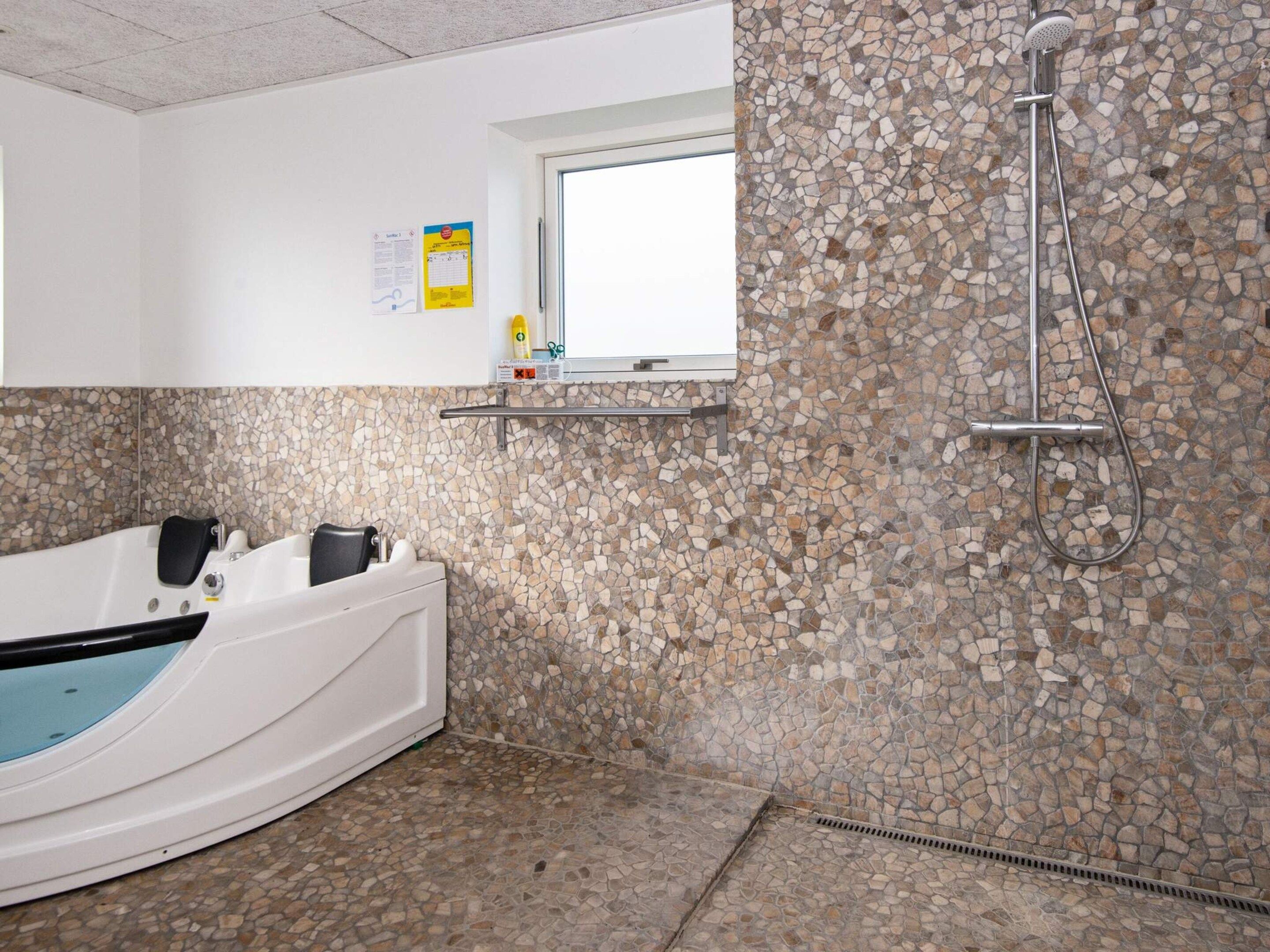 A bathroom with a bathtub, a shower, and a mosaic wall.