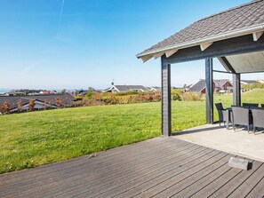 A covered outdoor seating area with a view of a residential neighborhood and a body of water.