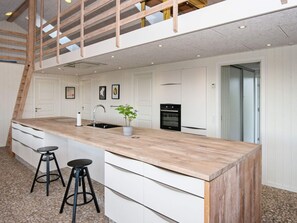 Uma cozinha moderna com bancada de madeira, pia, dois bancos e forno embutido.