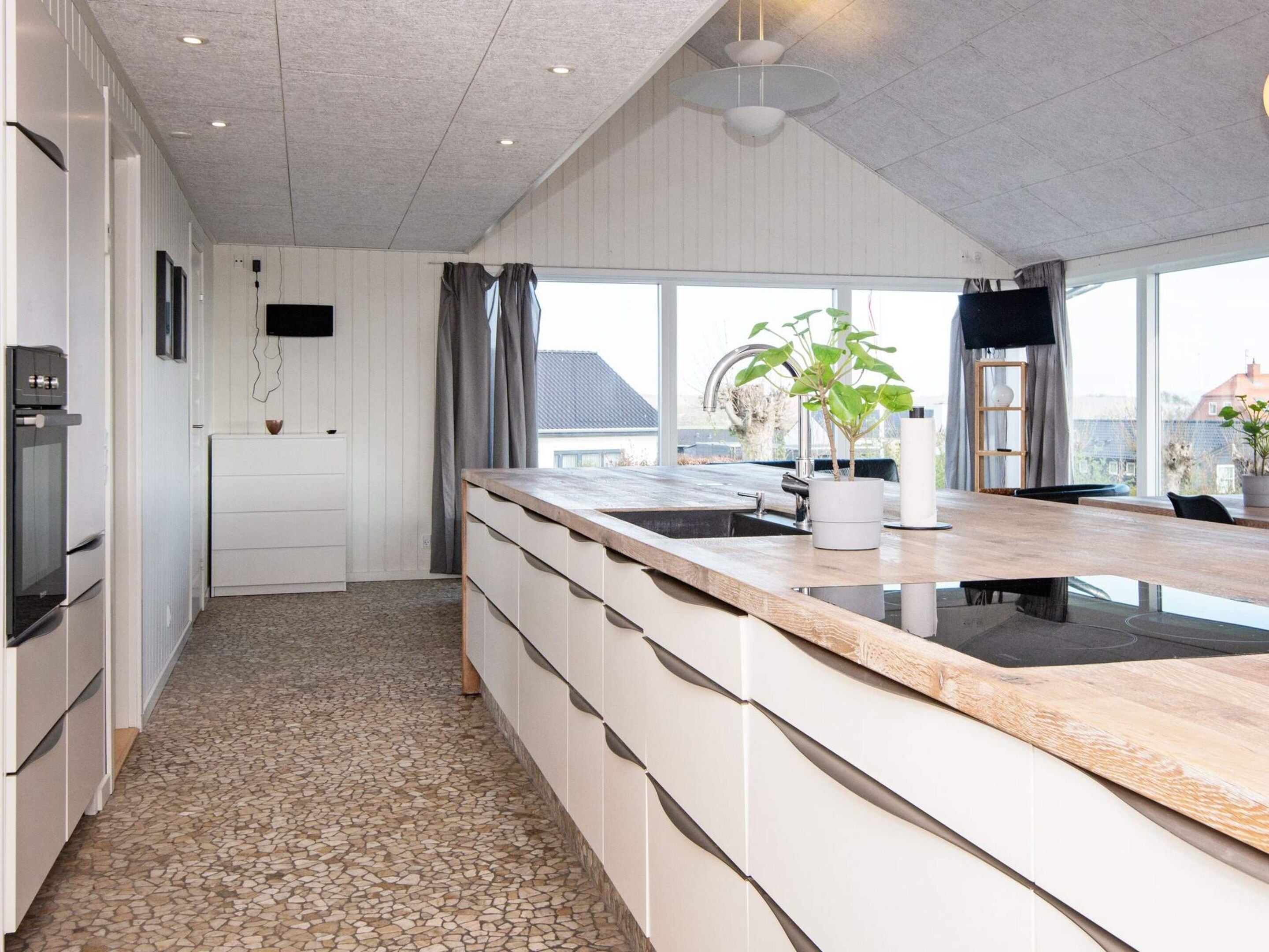 Une cuisine moderne dotée d’un grand îlot central, de meubles blancs et d’un sol carrelé en pierre.