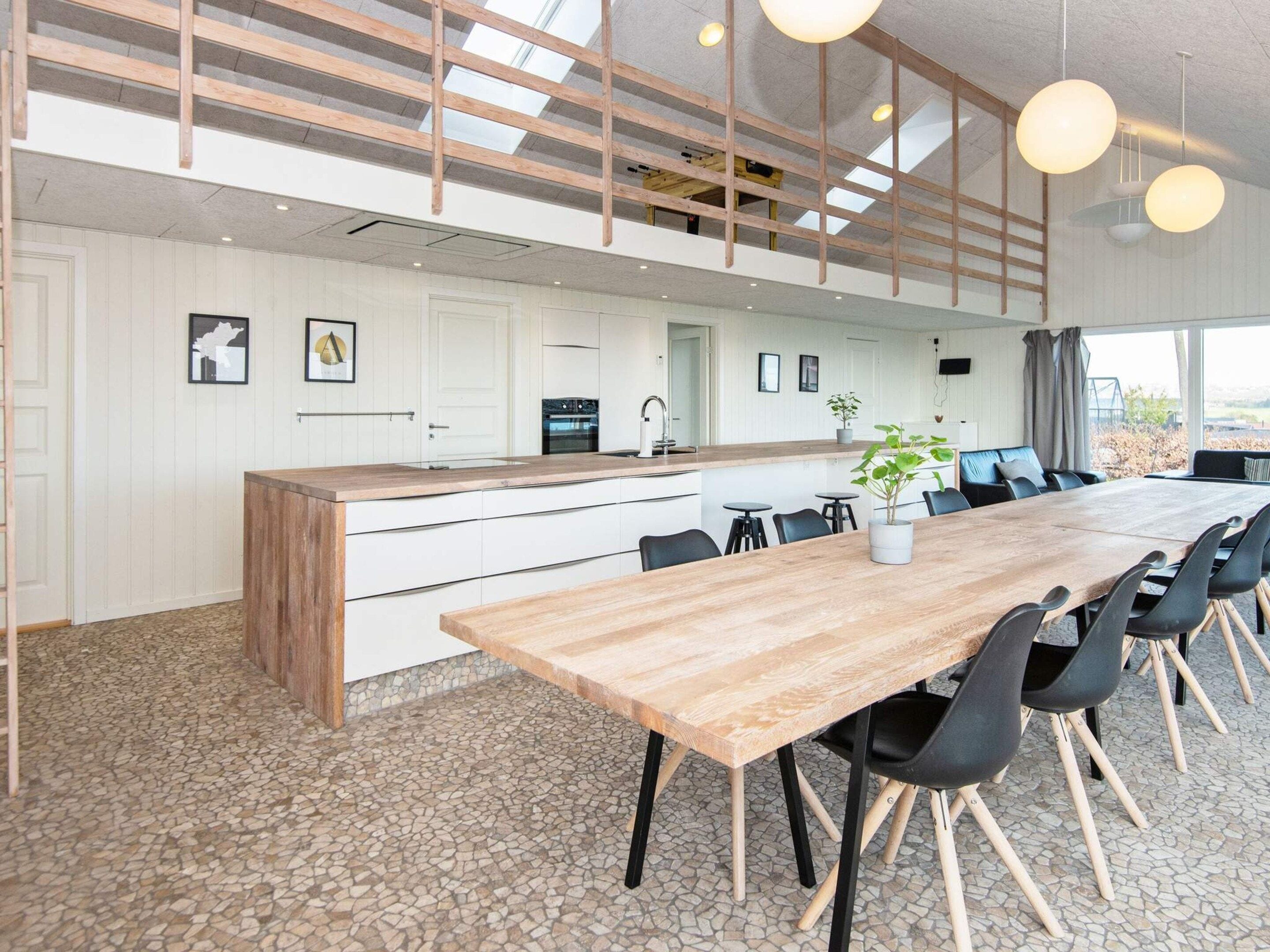 Una cucina moderna con un'isola centrale, un'area pranzo con un tavolo lungo e sedie, e vista sull'esterno.