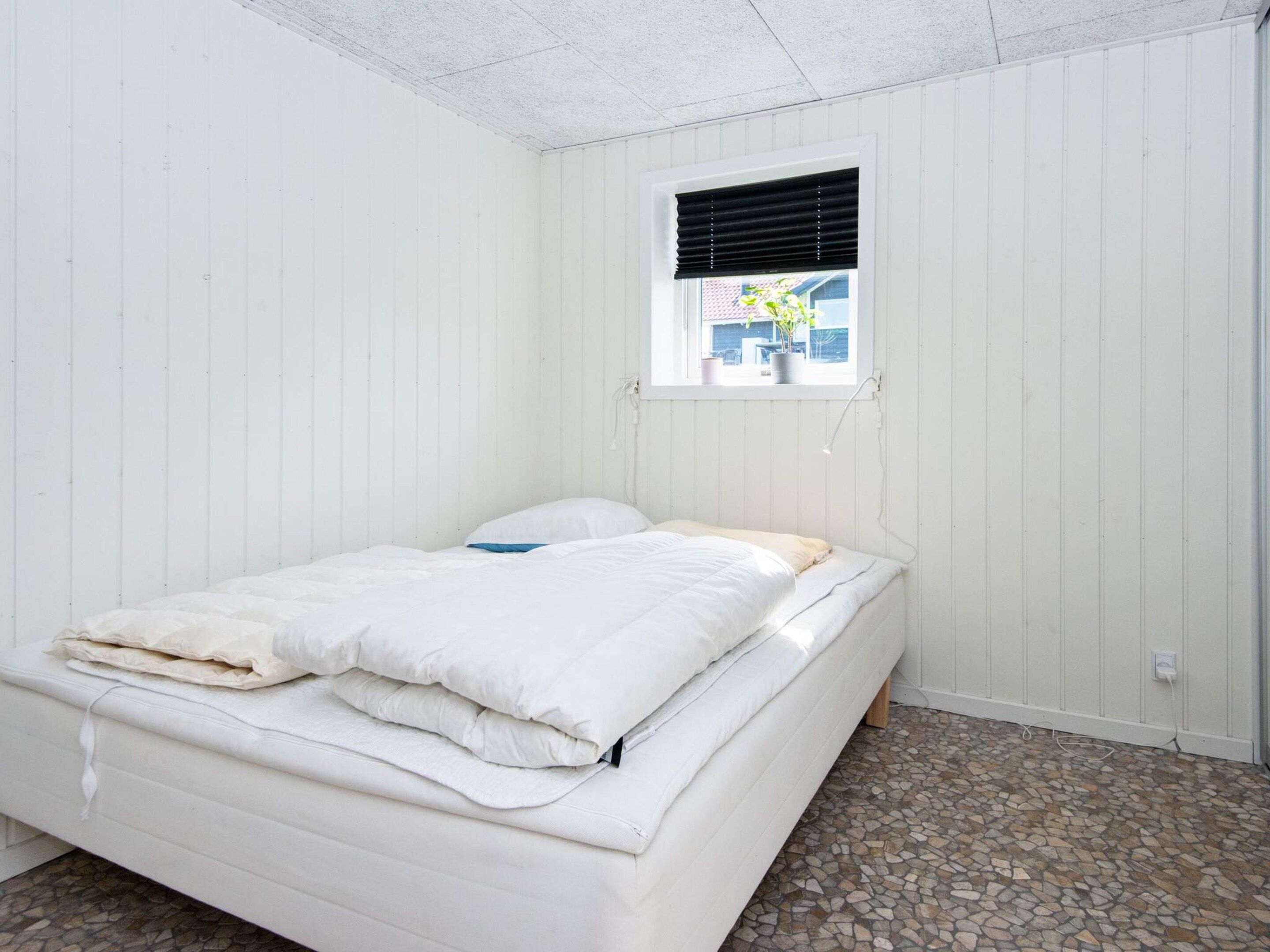 A single-bed room with a window, white walls, and a tiled floor.