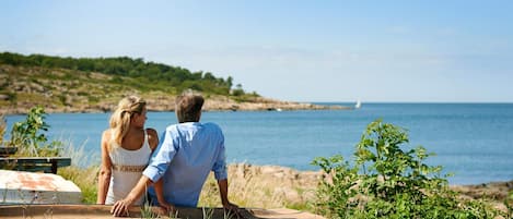 A couple sitting on a bench overlooking a coastal view with a rustic metal railing in the foreground.