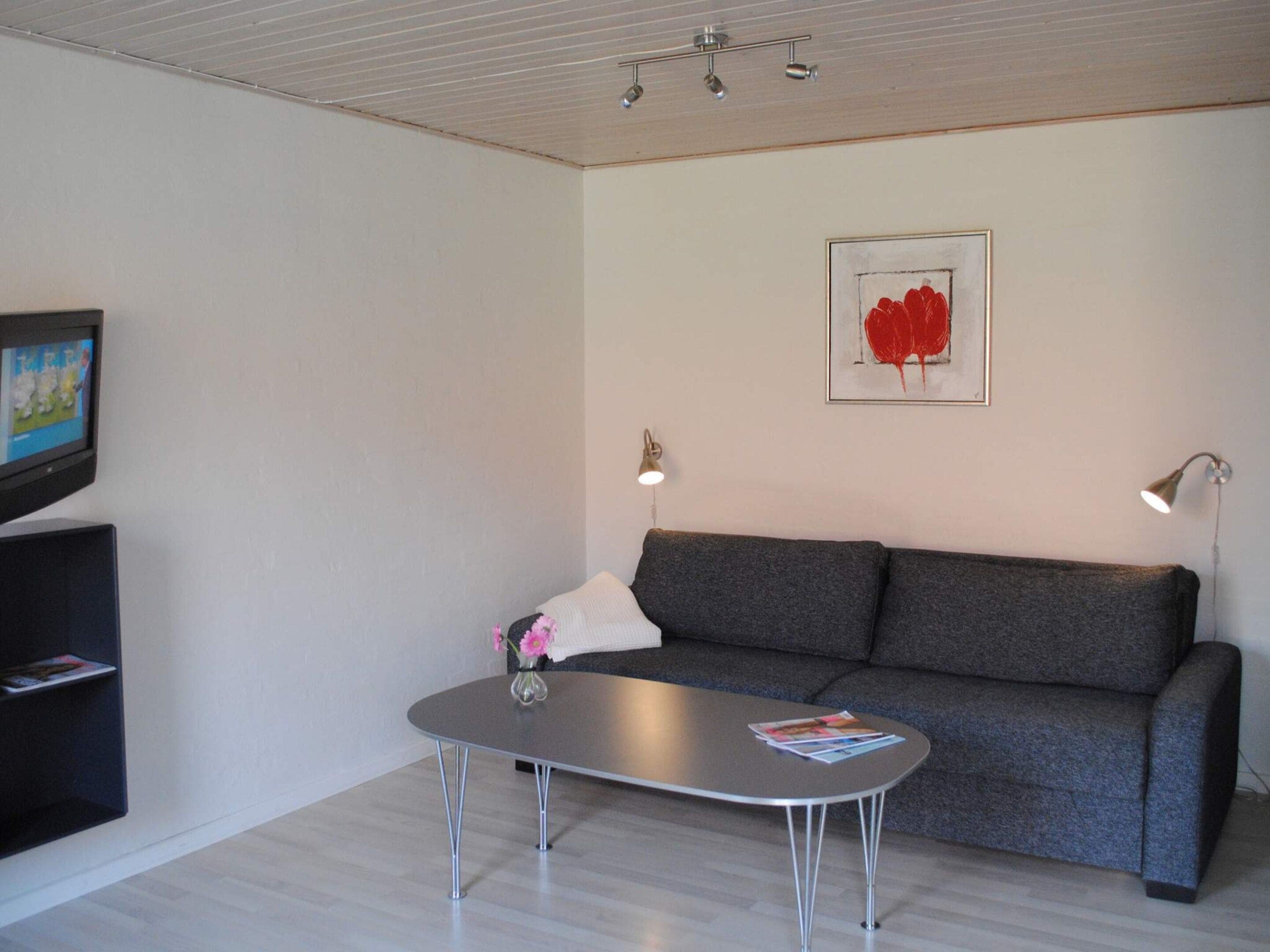 Una sala moderna con un sofá gris, una mesa de centro, un televisor sobre un mueble bajo y una obra de arte enmarcada en la pared.