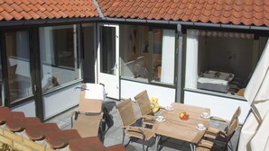 A covered patio with a tiled roof, a dining table with chairs, and a bed visible through the glass doors. - 2 Person Holiday Park Home in Allinge (Allinge)