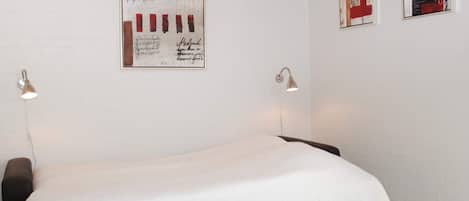 Een slaapkamer met een bed, twee wandlampen en twee ingelijste kunstwerken aan de muur.