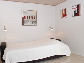 A bedroom with a bed, two wall-mounted lamps, and two framed artworks on the wall.