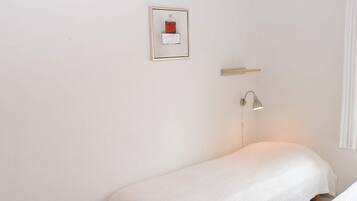 Una habitación pequeña y sencilla con cama, mesita de noche, lámpara y un cuadro enmarcado en la pared.