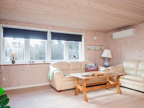 A cozy living room with a wooden ceiling, a beige sofa, a wooden coffee table, and a window with a view of trees. - 7 Person Holiday Home in Ulfborg (Ulfborg)