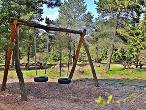 A wooden swing set with two swings, surrounded by trees and a picnic table in a park.