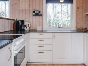A kitchen with white cabinets, a coffee maker, and a window with a view of trees.