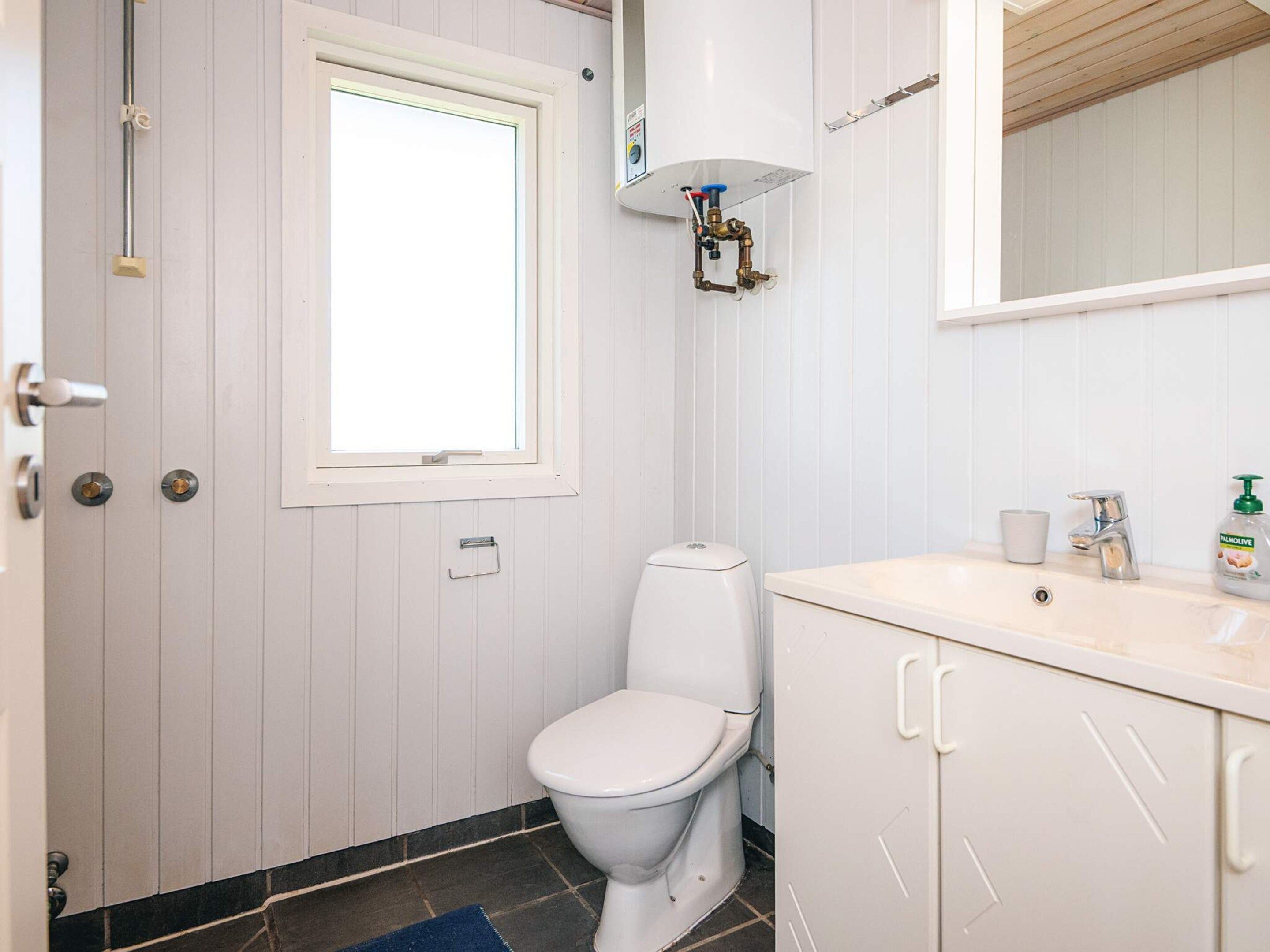 Un baño con inodoro, lavabo, espejo y ventana.