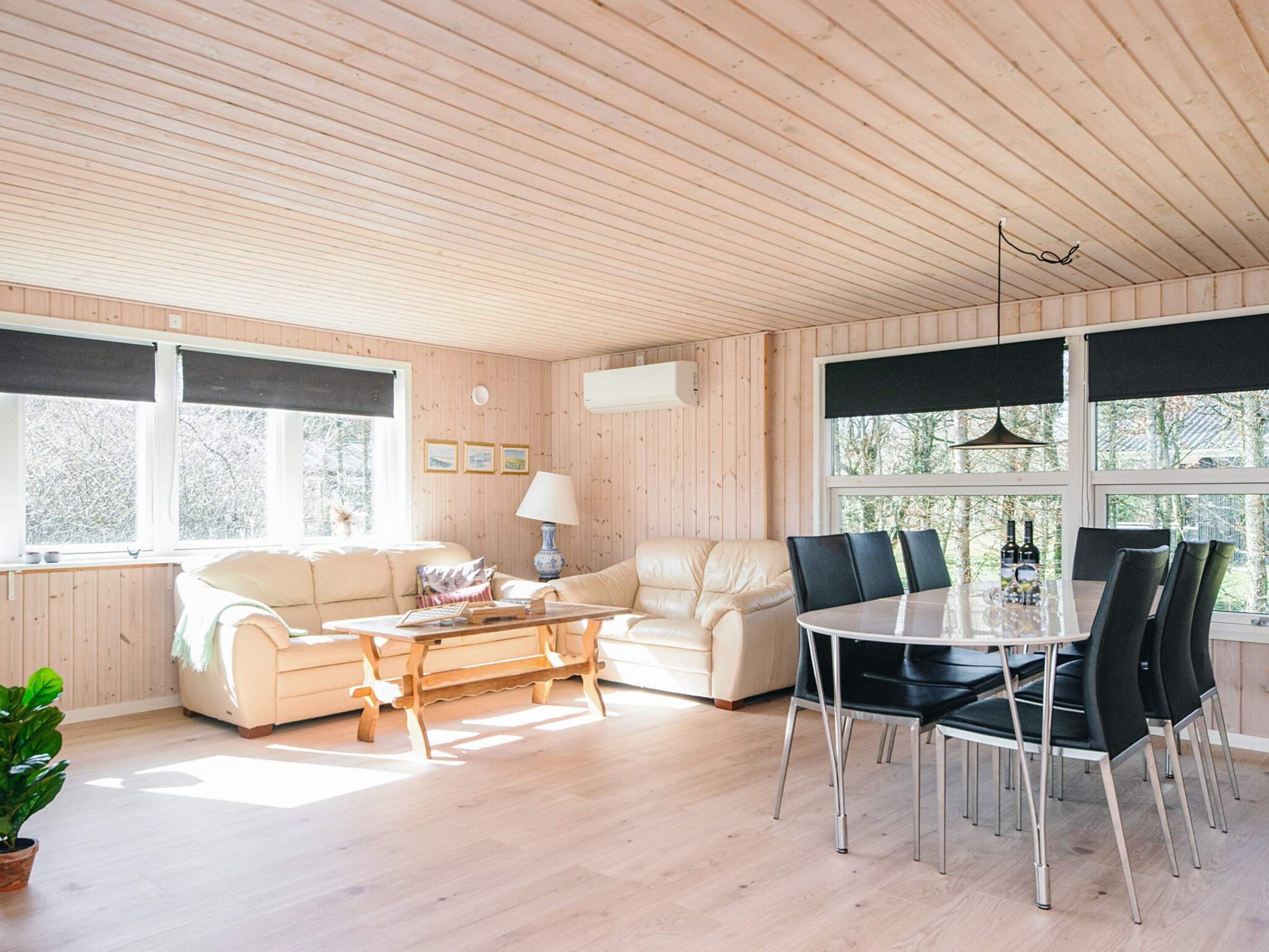 L’intérieur d’un chalet accueillant, avec un plafond en bois, un canapé, une table à manger avec des chaises et de grandes fenêtres.