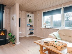 Ein gemütliches Zimmer mit Kaminofen, Bücherregal, Fenster mit Aussicht und einem Holztisch mit Schachspiel.
