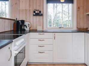 Una cocina con armarios blancos, una cafetera y un ventanal con vistas a árboles.