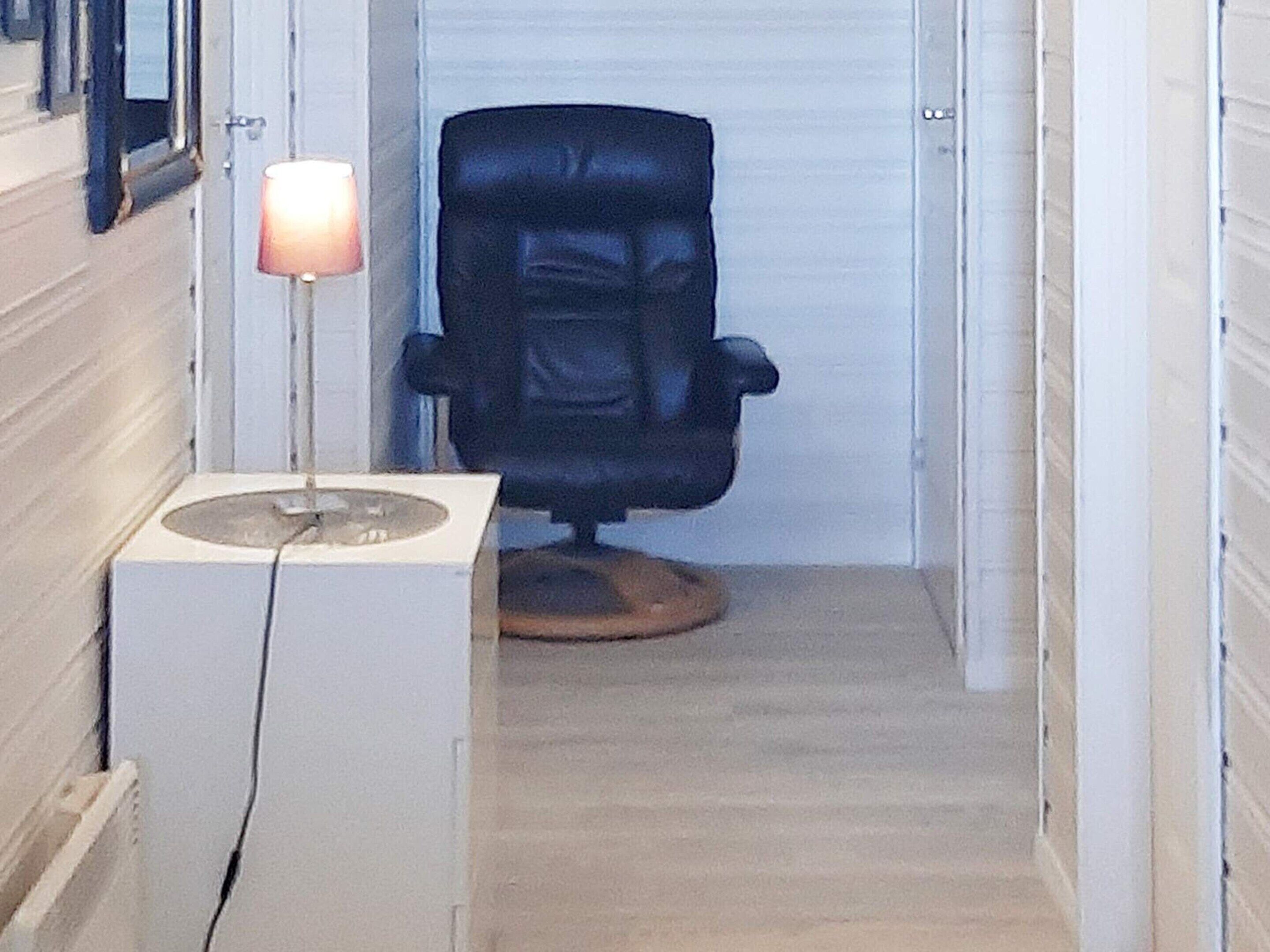 A narrow hallway with a black office chair and a white cabinet with a lamp.