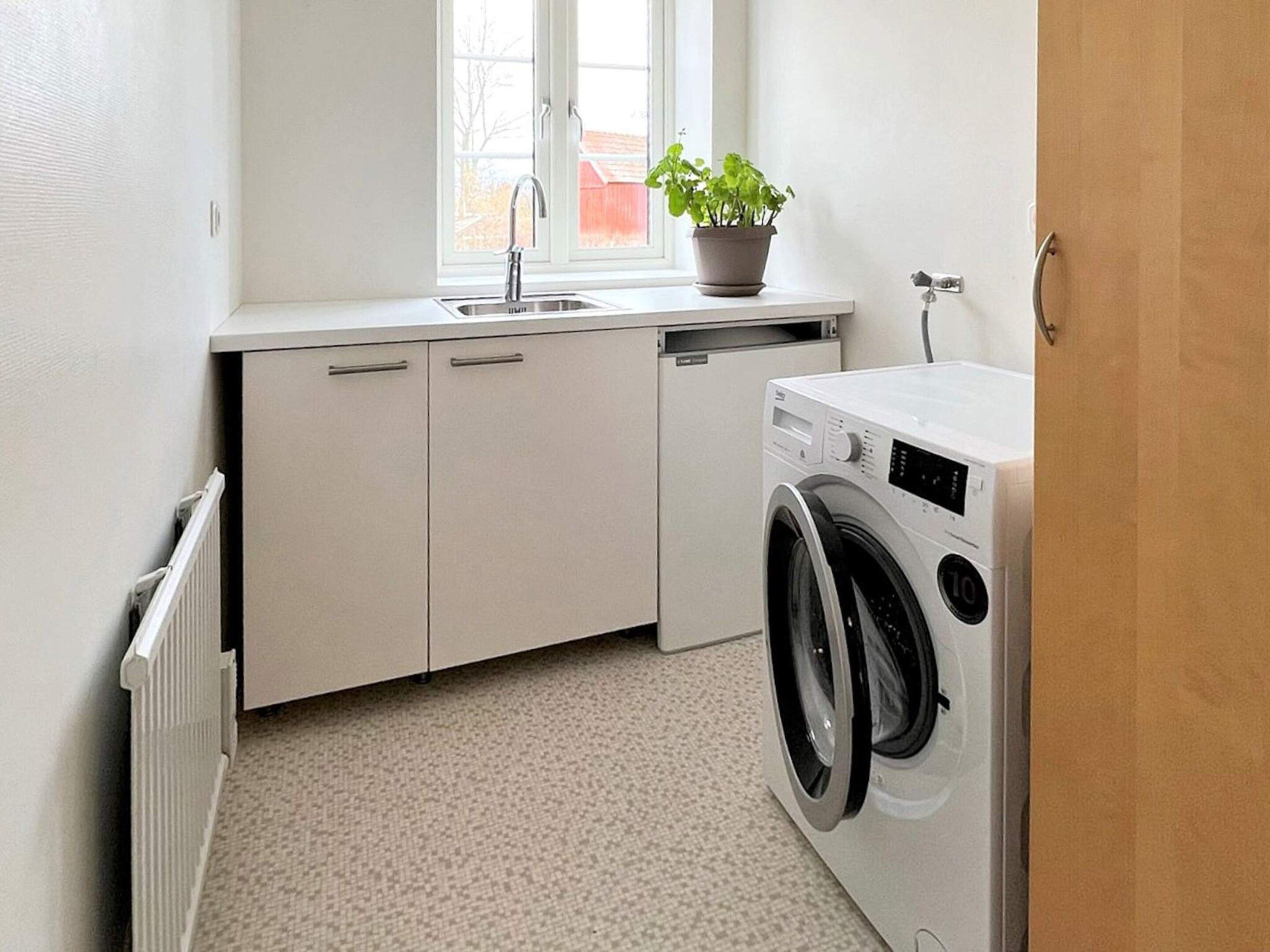 A compact kitchen with a built-in washing machine, a window with a plant, and a radiator.