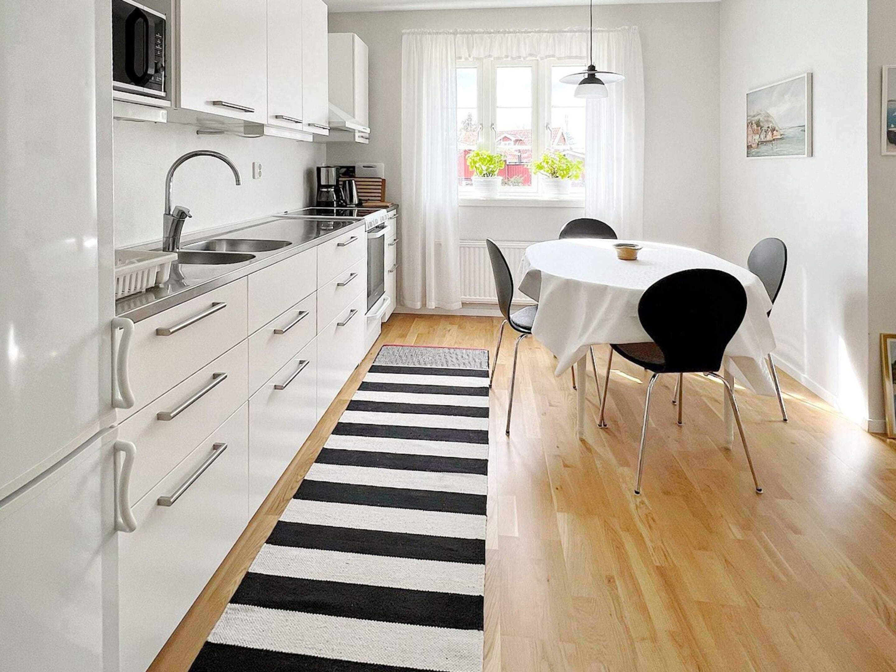 A modern kitchen with white cabinets, a black and white striped rug, and a dining area with a table and chairs.