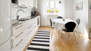 Et moderne køkken med hvide skabe, en stribet måtte i sort og hvid, samt et spiseområde med bord og stole.