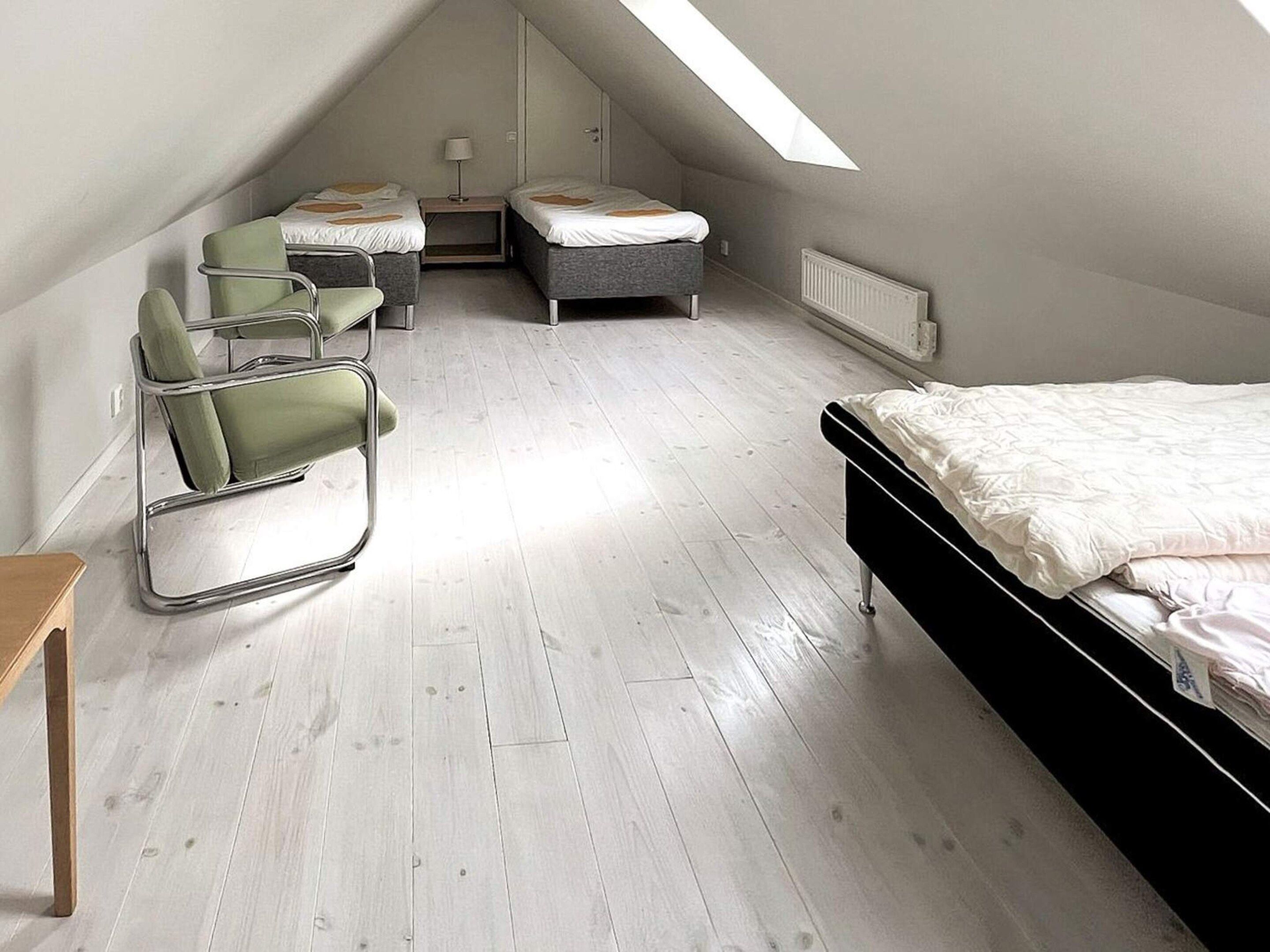 A room with a sloped ceiling, a bed, two chairs, a small table, and a radiator.