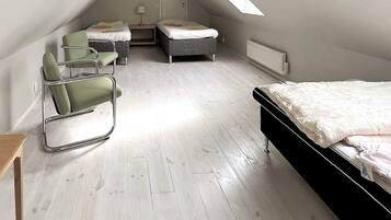 A room with a sloped ceiling, a bed, two chairs, a small table, and a radiator.